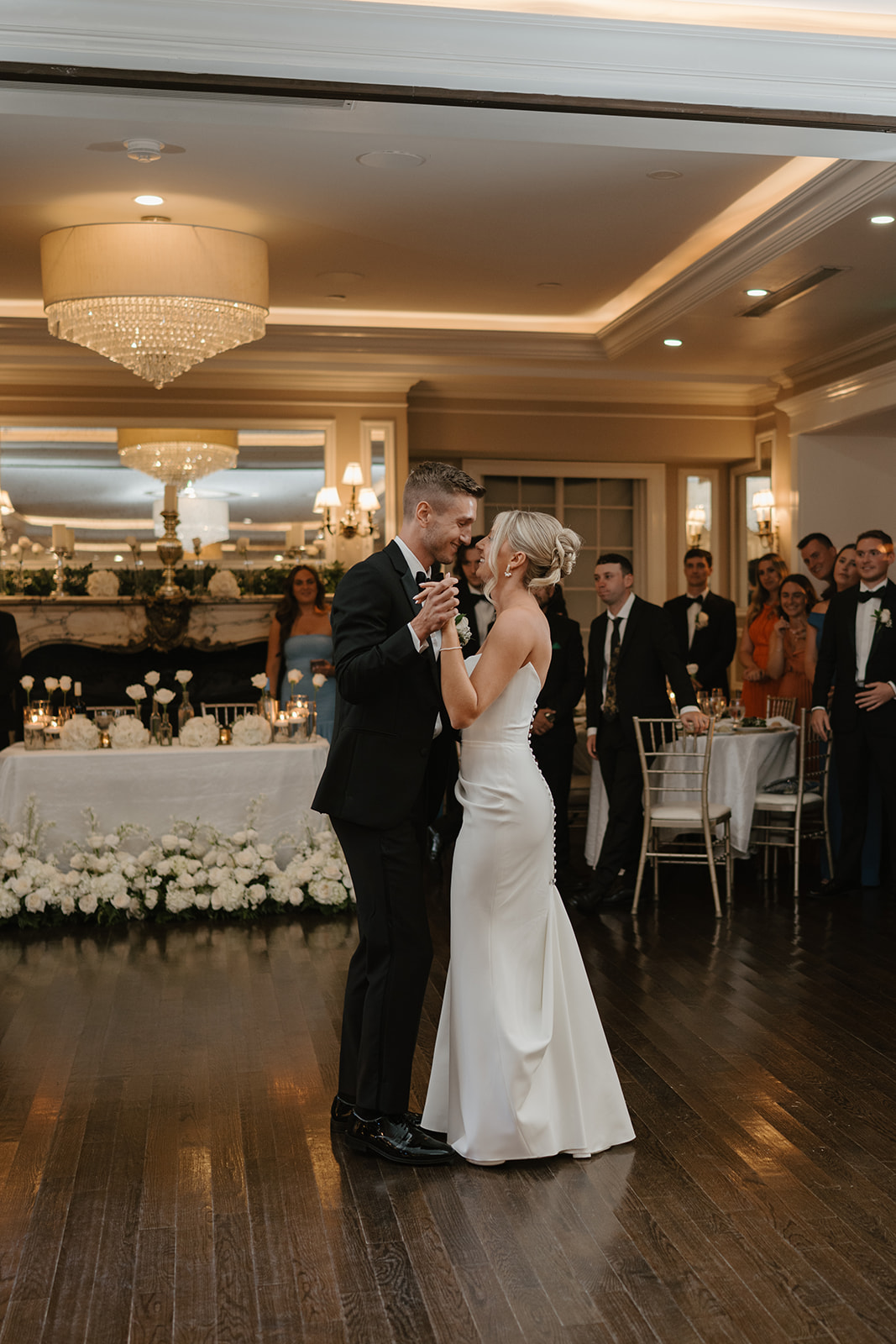 Newlyweds smile warmly at each other while sharing their romantic first dance in the ballroom.
